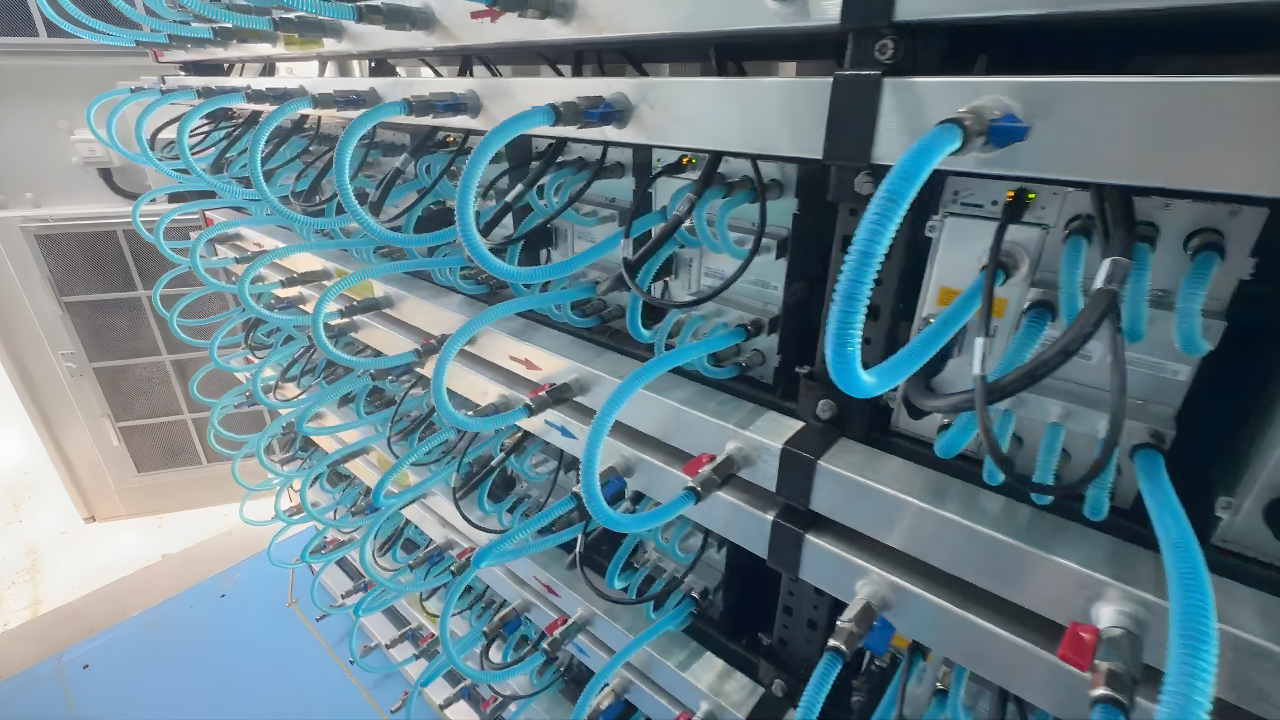 Close-up of a professional liquid-cooled Bitcoin mining rack showing intricate blue tubing and high-density ASIC miner deployment in a data center.