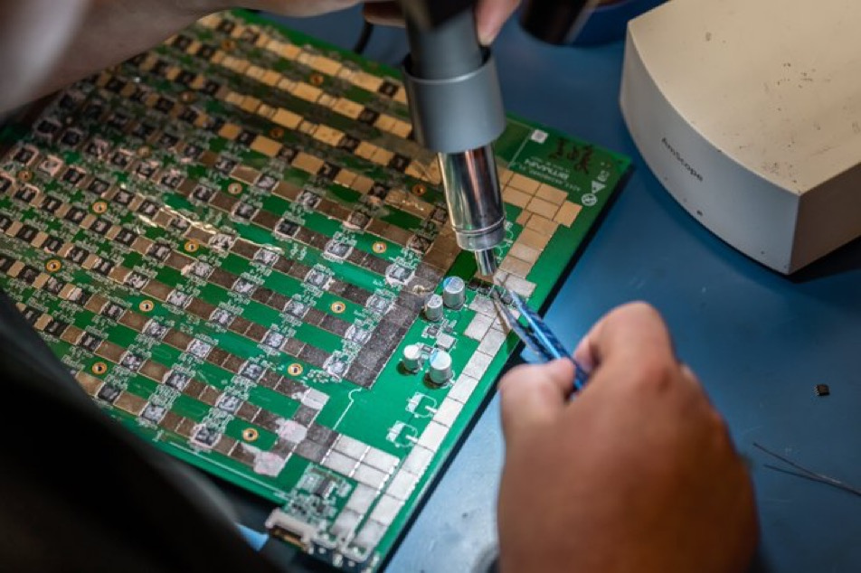 A technician performing a precision hash board repair on a Bitcoin ASIC miner at a certified repair center.